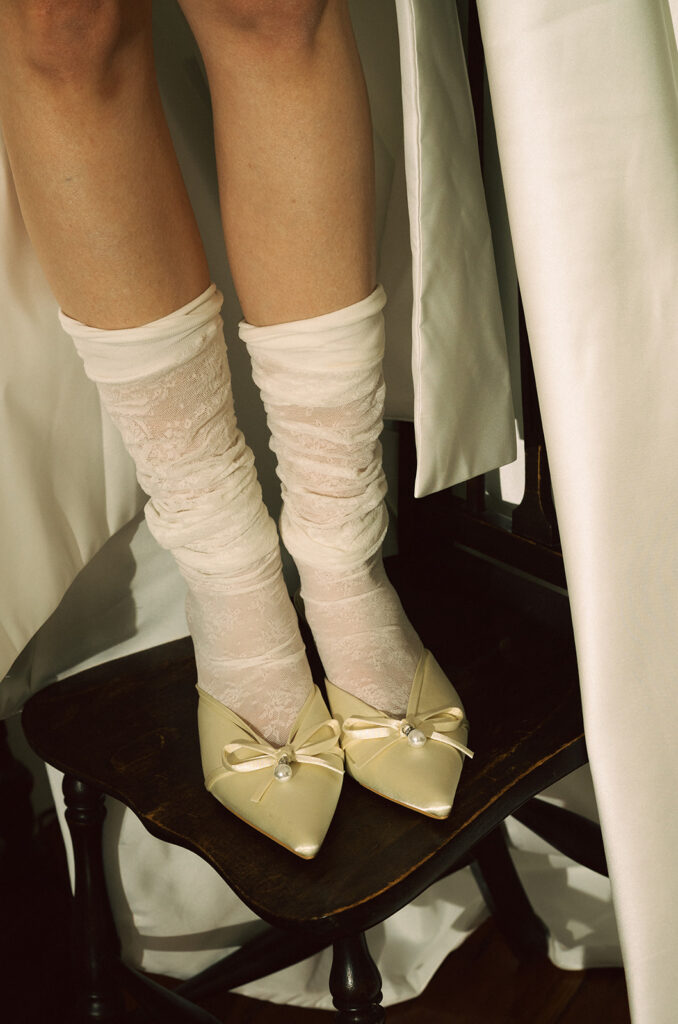 Close up shot of a bride wearing stockings and heels while standing on a chair. 