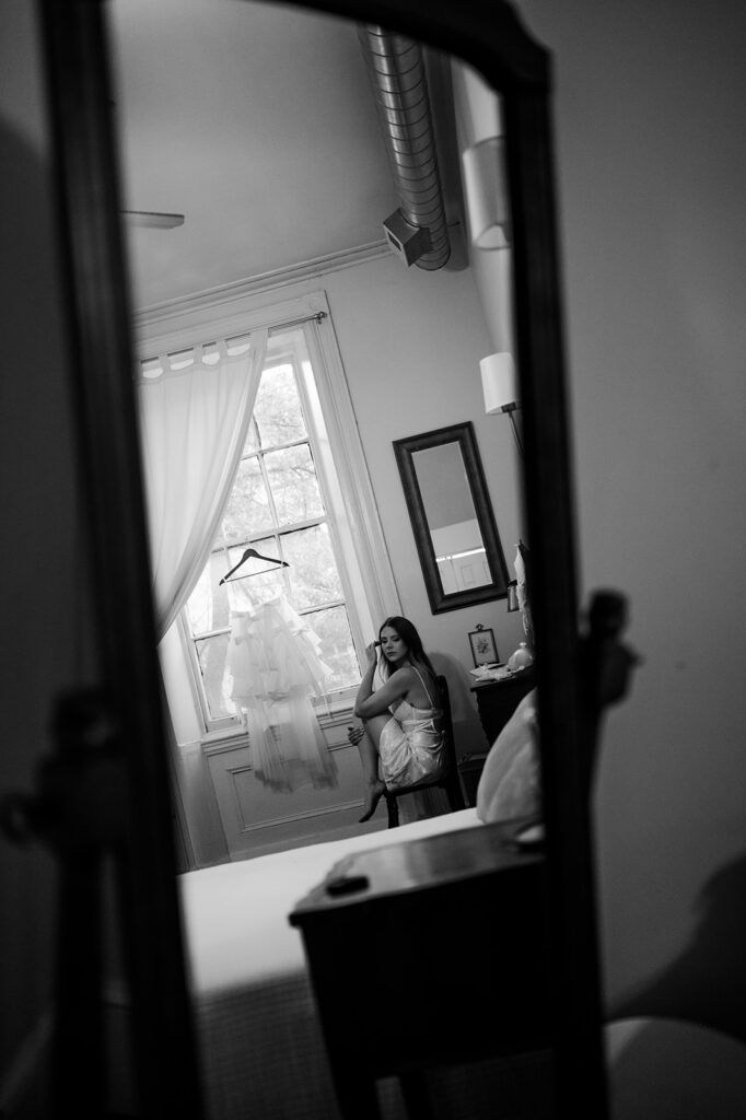 Black and white cinematic style photo of a bride sitting in a chair by a window at Vaux Studio in Philadelphia.