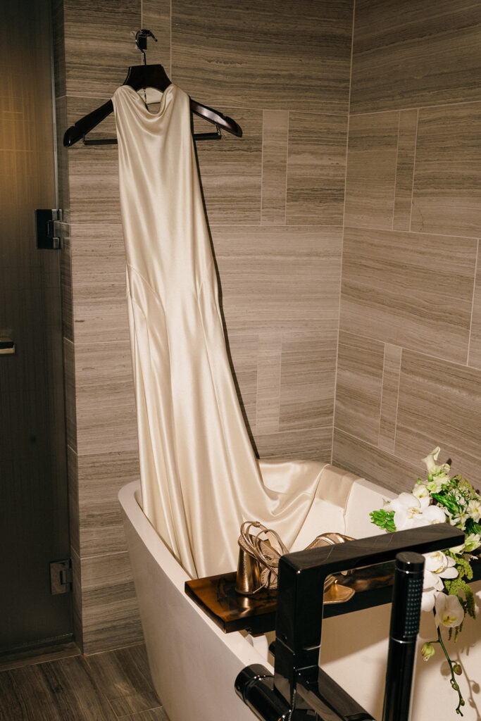 Brides long elopement dress hanging in her hotel bathroom. 