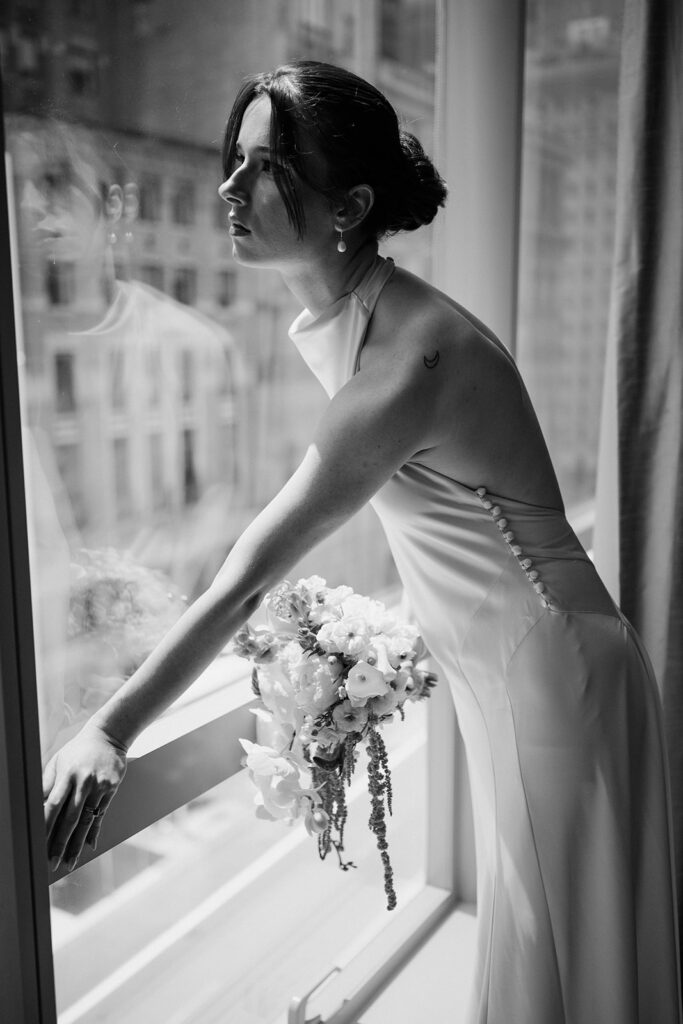 Black and white photo of  bride looking out her hotel window in NYC.