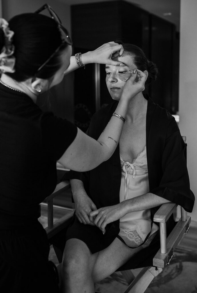 Black and white photo of the bride getting her makeup done. 