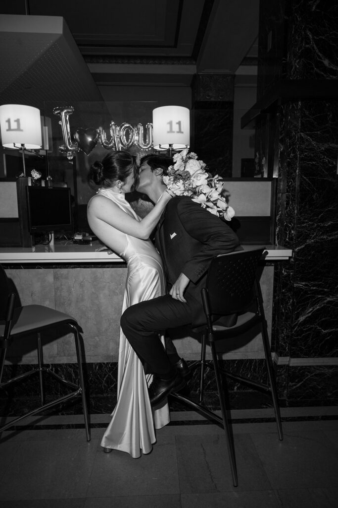 Black and white photo of a bride and groom kissing at the front desk during their NYC City Hall elopement.