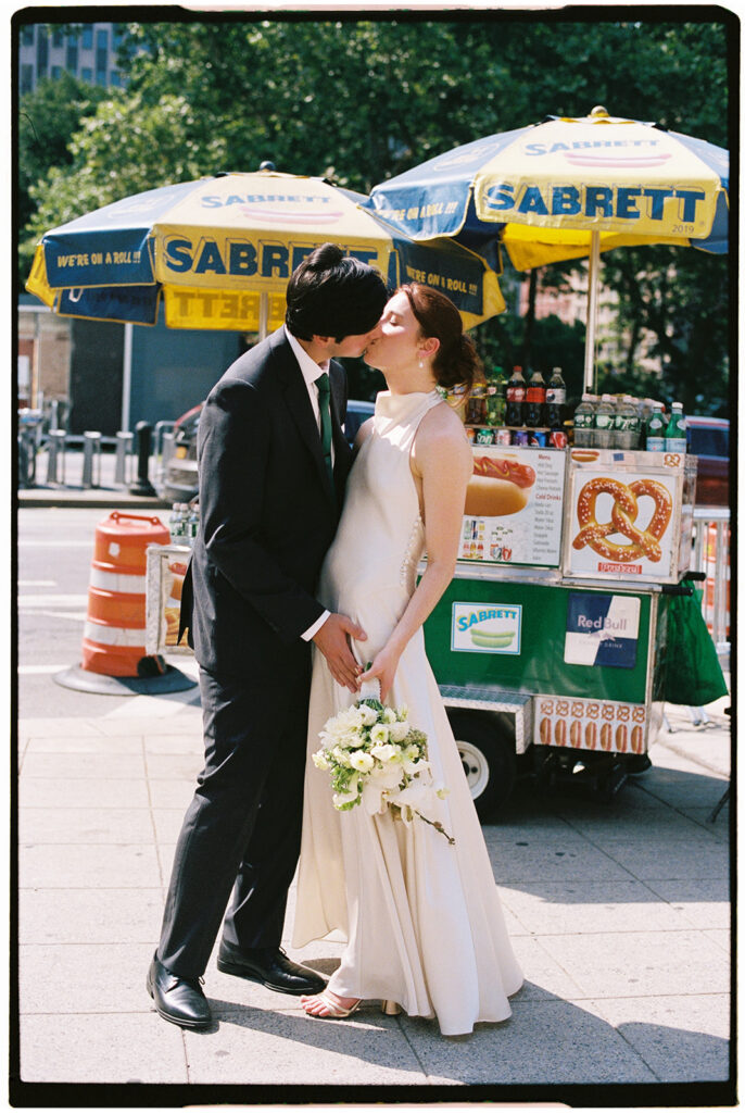 Film photo of a couple kissing downtown NYC during their elopement in front of a hotdog cart. 