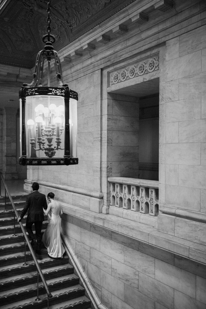 Black and white photo of a couple walking up a stairway at The New York Public Library. 